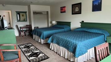 A hotel room with two beds, a desk, a chair, a small table, and a door.