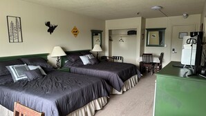 A hotel room with two beds, a desk, a chair, a mirror, and a coat rack. - The Kenai Inn (Kenai)