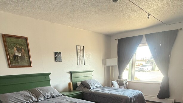 A bedroom with two beds, a green headboard, a window with curtains, and a bear-themed rug. - The Kenai Inn (Kenai)