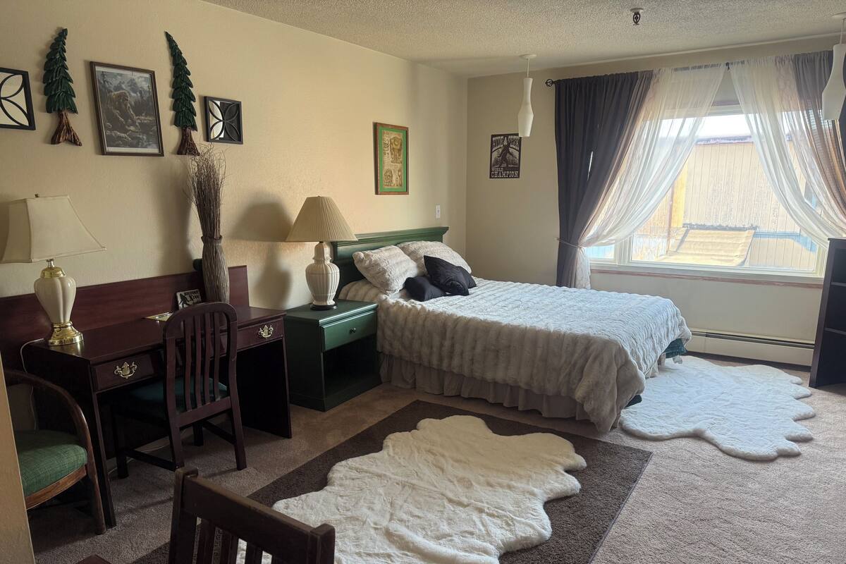 Hotellihuone, jossa on sänky, työpöytä, tuoli, lamppu ja ikkuna, jossa on verhot.