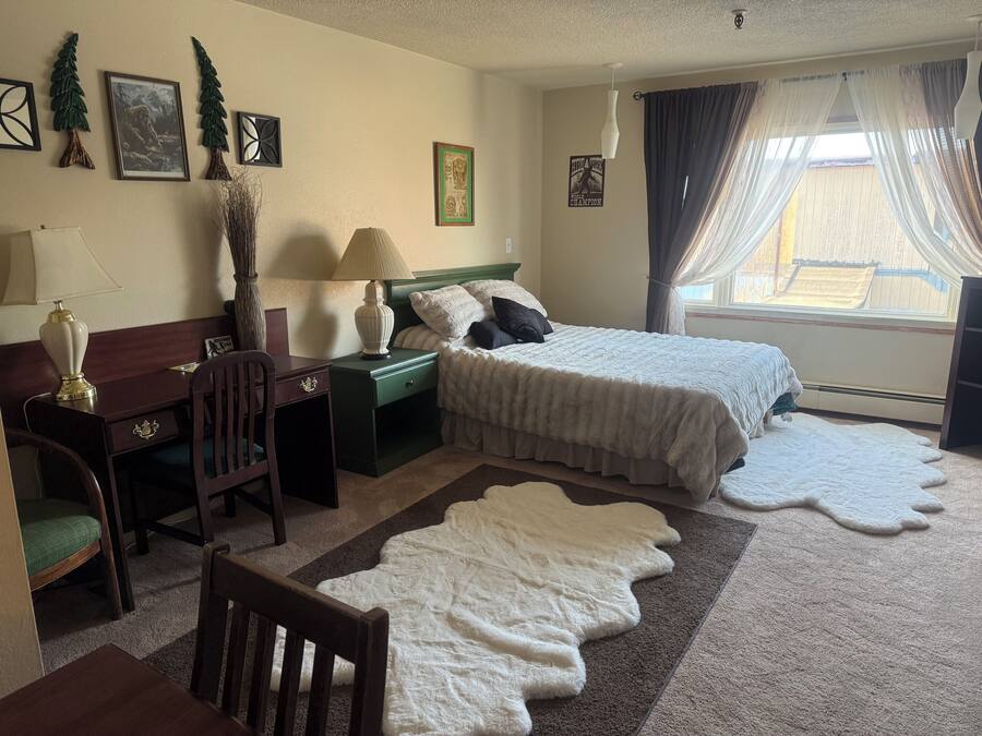 Ein Hotelzimmer mit Bett, Schreibtisch, Stuhl, Lampe und einem fensterbepflanzten Fenster.