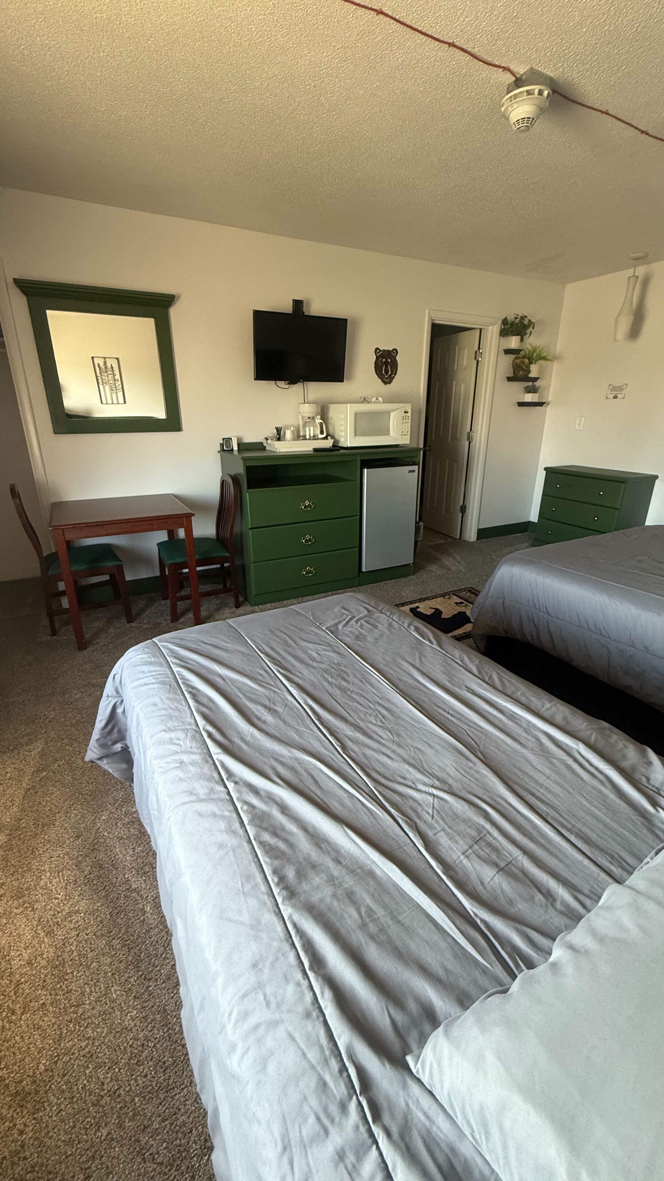 Ein Schlafzimmer mit zwei Betten, einem Schreibtisch mit Stuhl, einer Mikrowelle, einer Kaffeemaschine und einem Fernseher an der Wand.