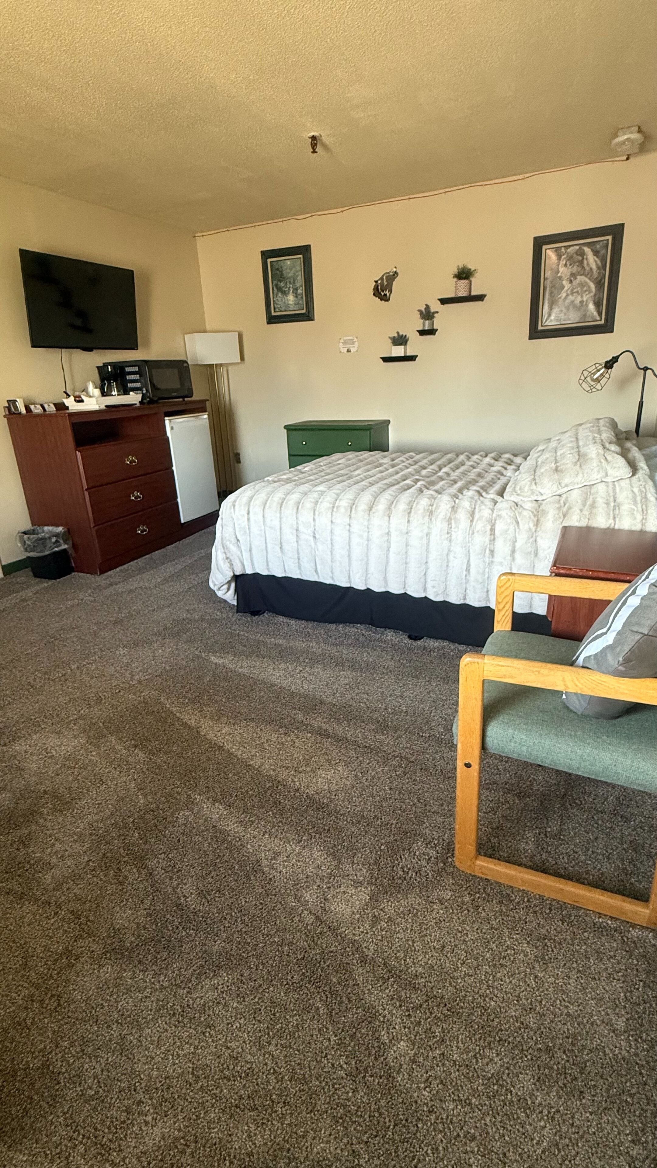 Un dormitorio con una cama, un escritorio con una computadora, una silla y un televisor en la pared.