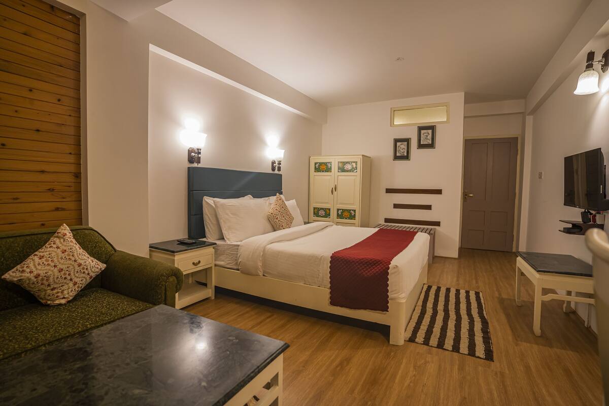 A bedroom with a bed, nightstands, a dresser, a television, and a desk.