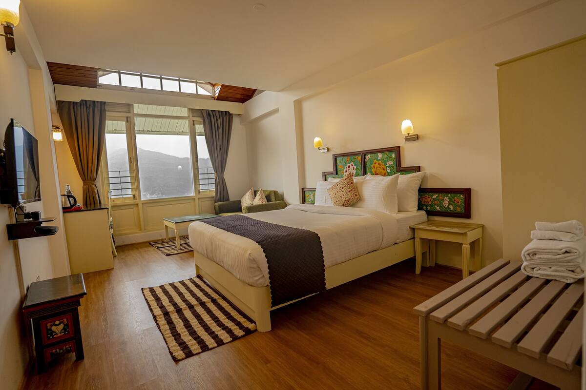 A bedroom with a large bed, bedside tables, a TV, and a window with curtains.