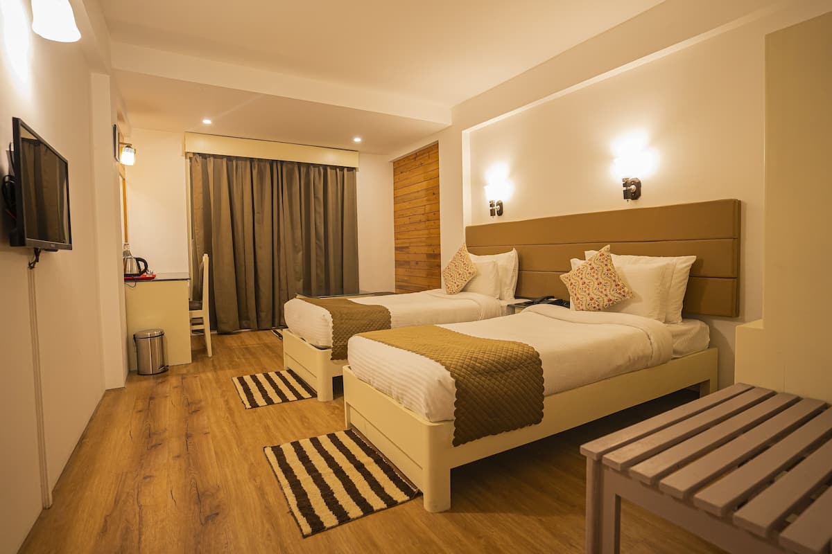 A hotel room with two beds, a TV, a wooden wall, a trash bin, and a small table.