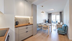 A modern kitchen with a marble backsplash, wooden countertop, and built-in cabinets. There is a dining area with a table and chairs, and a sofa in the living area. - Apartamenty Sun & Snow Plażowa Park (Dziwnów)