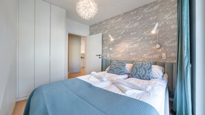 A modern bedroom with a large bed, a wardrobe, and a bathroom visible through an open door. - Apartamenty Sun & Snow Plażowa Park (Dziwnów)