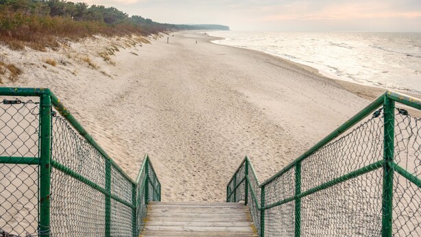 A wooden staircase leading to a sandy beach with a fence on either side. - Apartamenty Sun & Snow Plażowa Park (Dziwnów)