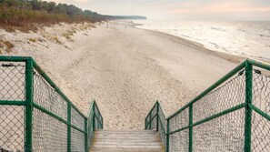 A wooden staircase leading to a sandy beach with a fence on either side.