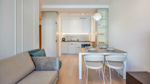 A modern kitchen with white cabinets, a dining table with four chairs, and a built-in oven. - Apartamenty Sun & Snow Plażowa Park (Dziwnów)