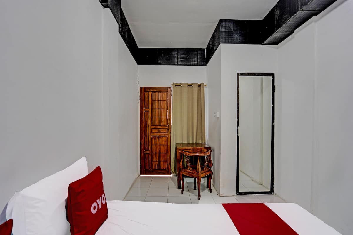 A hotel room with a bed, a wooden chair, a mirror, and a door.