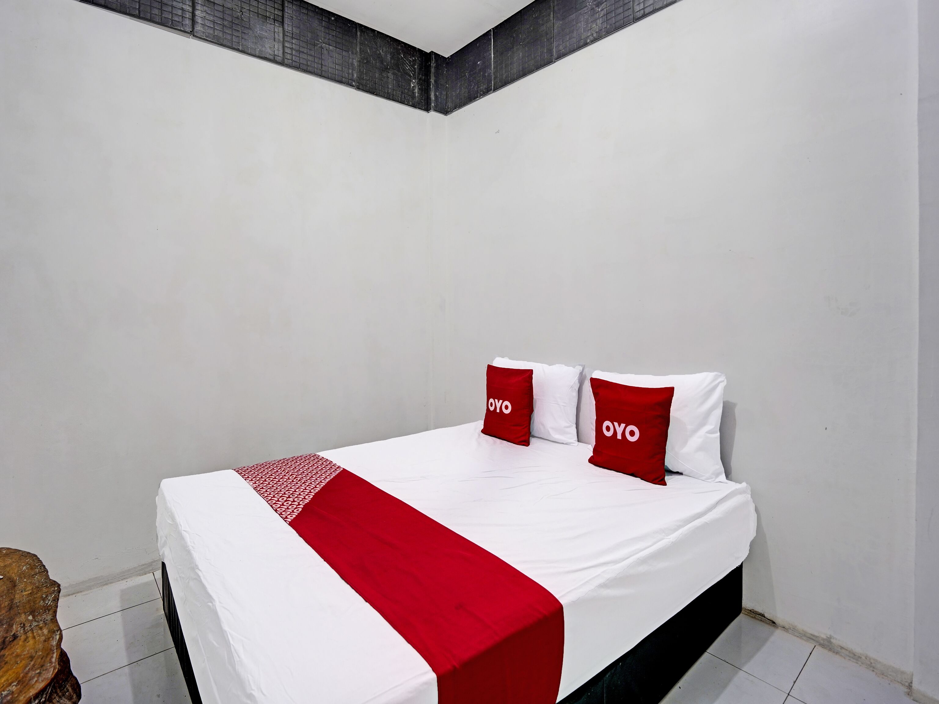 Una cama con ropa de cama blanca y roja, dos almohadas con la palabra “OYO” y una manta estampada en rojo y blanco.