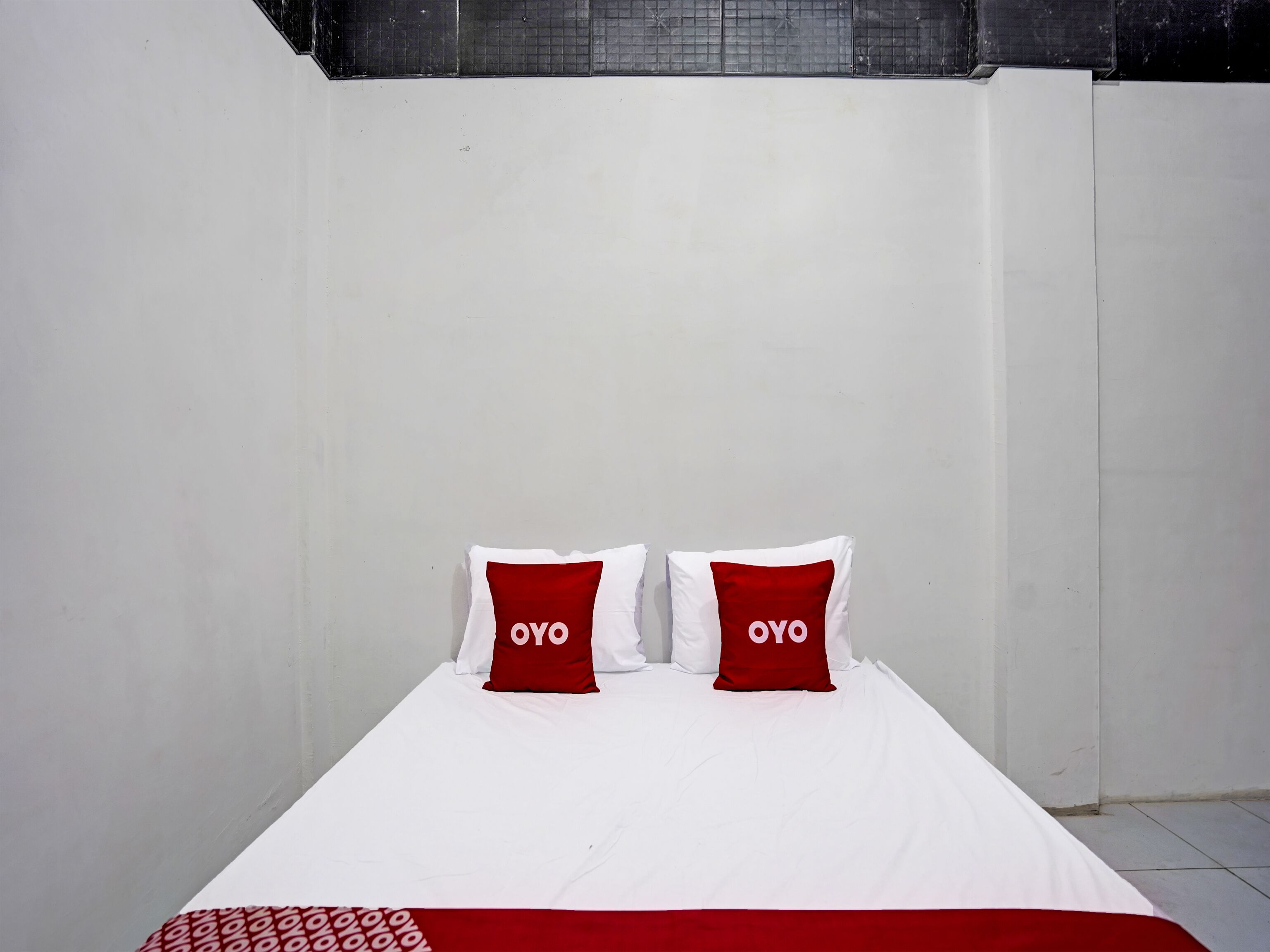 Una cama individual con ropa de cama blanca y dos almohadas rojas con el texto 'OYO'.