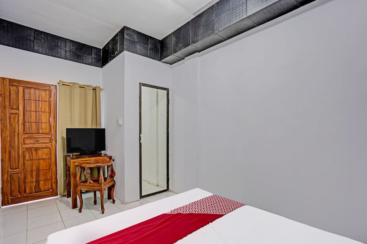 A hotel room with a bed, a wooden wardrobe, a television on a wooden stand, and a mirror.