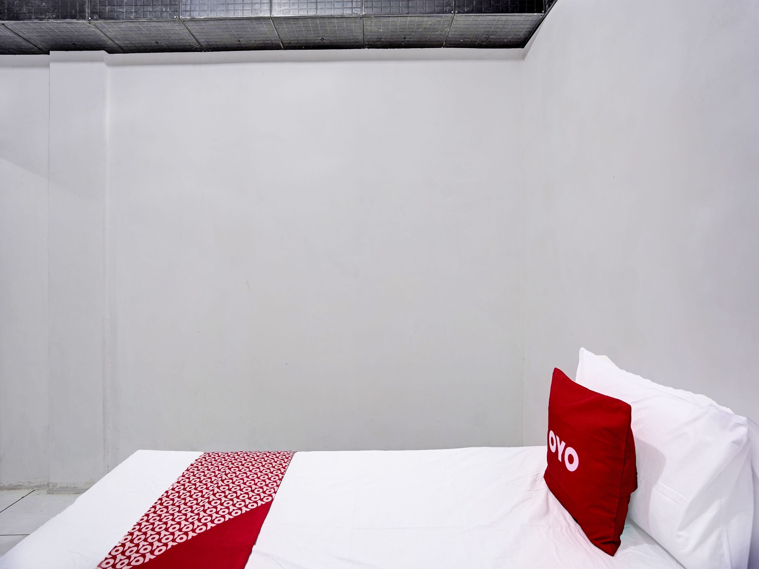 Un letto singolo con copriletto bianco e rosso, un cuscino rosso con la scritta "YOYO" e un lucernario sopra.