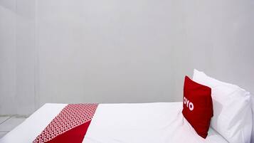 Un letto singolo con copriletto bianco e rosso, un cuscino rosso con la scritta "YOYO" e un lucernario sopra.