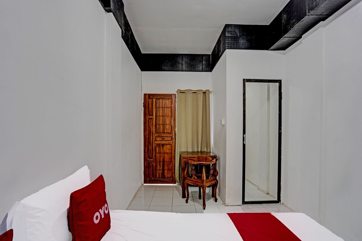 Quarto de hotel com uma cama, uma cadeira de madeira, um espelho e uma porta.