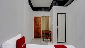 Una habitación de hotel con una cama, una silla de madera, un espejo y una puerta.