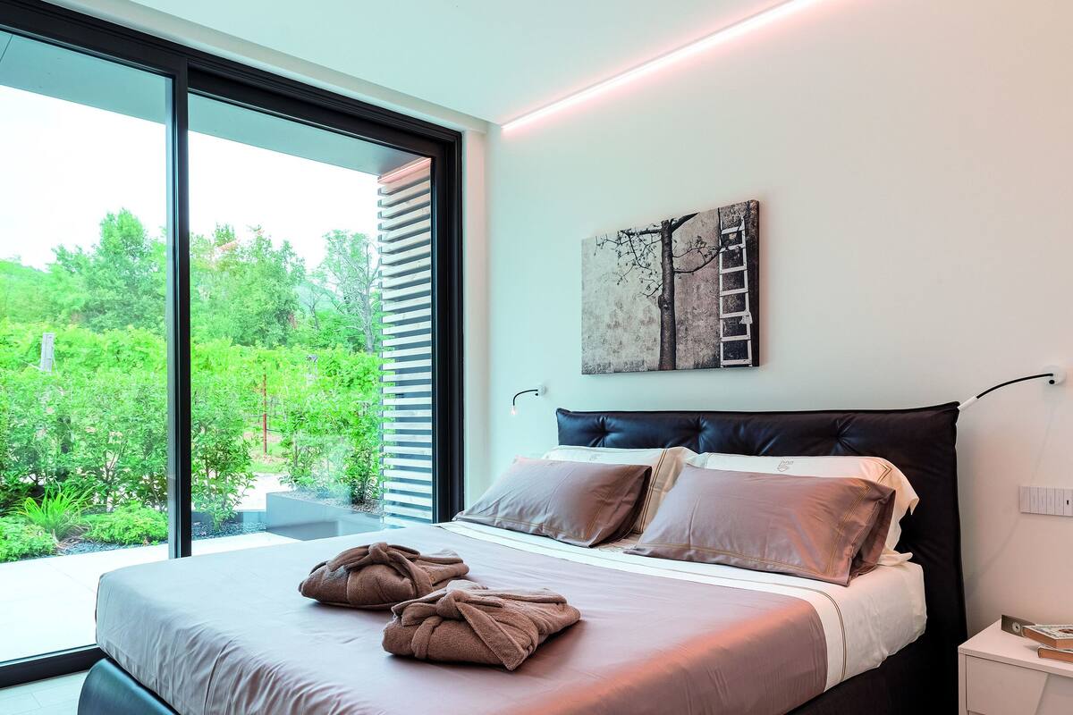 Et moderne soveværelse med en stor seng og udsigt til grøn vegetation, samt en lampe fastgjort til loftet.
