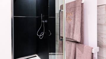 A modern bathroom with a glass shower enclosure, a white sink, and a towel rack with towels.