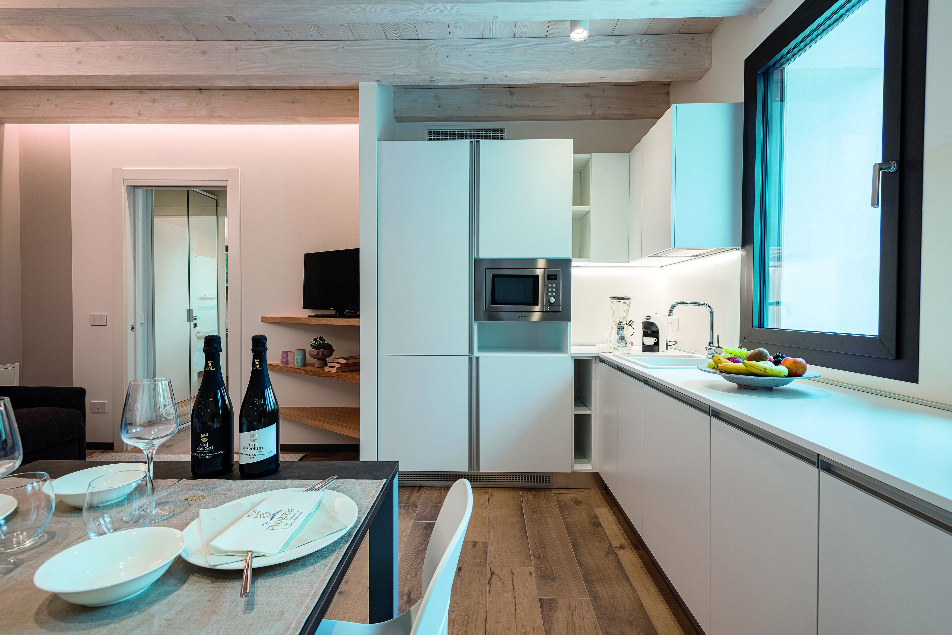 Una cucina moderna con mobili bianchi, un forno a microonde e una ciotola di frutta sul piano di lavoro.