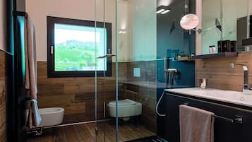 Un baño moderno con cabina de ducha de vidrio, un espejo grande y vistas a un paisaje verde a través de una ventana.