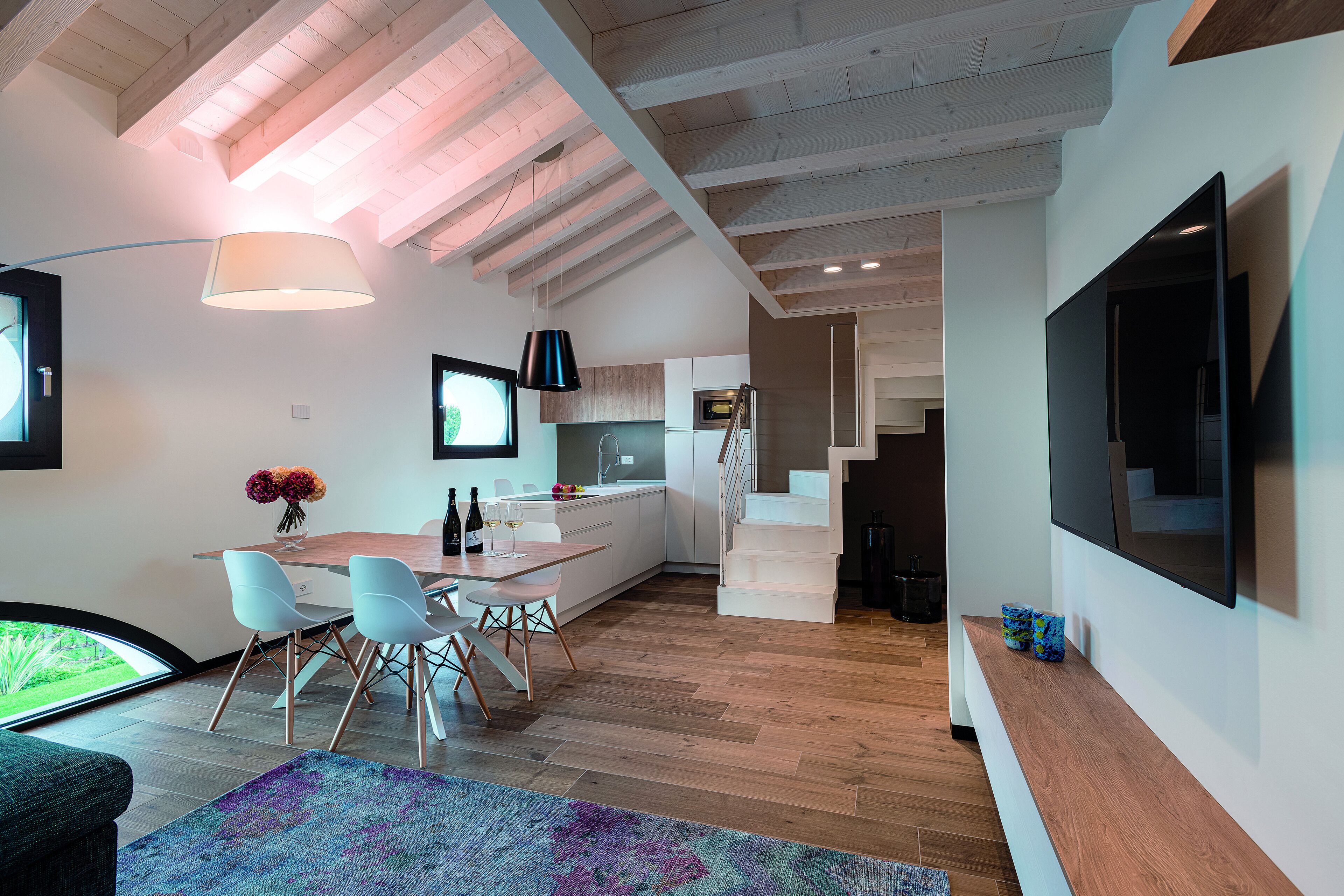 Cocina moderna con armarios blancos, comedor con mesa y sillas, y una escalera que sube a otro nivel.