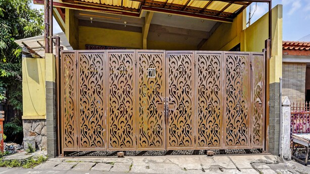 A gated entrance with intricate metalwork, a stone wall, and a yellow building in the background. - Hotel O Raffa Residence Syariah (Surabaya)