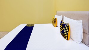 A hotel room with a bed, two pillows with yellow and blue patterns, and a light-colored headboard. - Hotel O Raffa Residence Syariah (Surabaya)