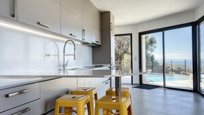 A modern kitchen with a large island, stainless steel appliances, and a view of a swimming pool. - Villa panoramic sea view, heated pool, Monticello, 4 bedrooms (Monticello)