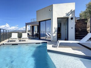 Un espace piscine moderne avec une eau d’un bleu limpide, des chaises longues blanches et une vue sur les montagnes.