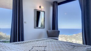 A bedroom with a large bed, a chair, a mirror, and a view of the sea. - Villa panoramic sea view, heated pool, Monticello, 4 bedrooms (Monticello)