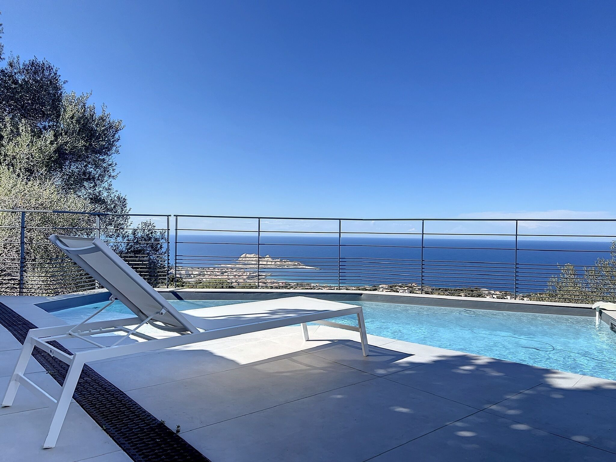 Un espace aménagé au bord de la piscine, avec des chaises longues et une vue sur l’océan.