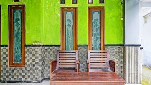 A wooden table with two chairs in front of a green wall with decorative windows. - Hotel O Fun Guesthouse Syariah (Mojokerto)