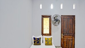 A small, simple room with a bed, two pillows, a fan, and a wooden door. - Hotel O Fun Guesthouse Syariah (Mojokerto)