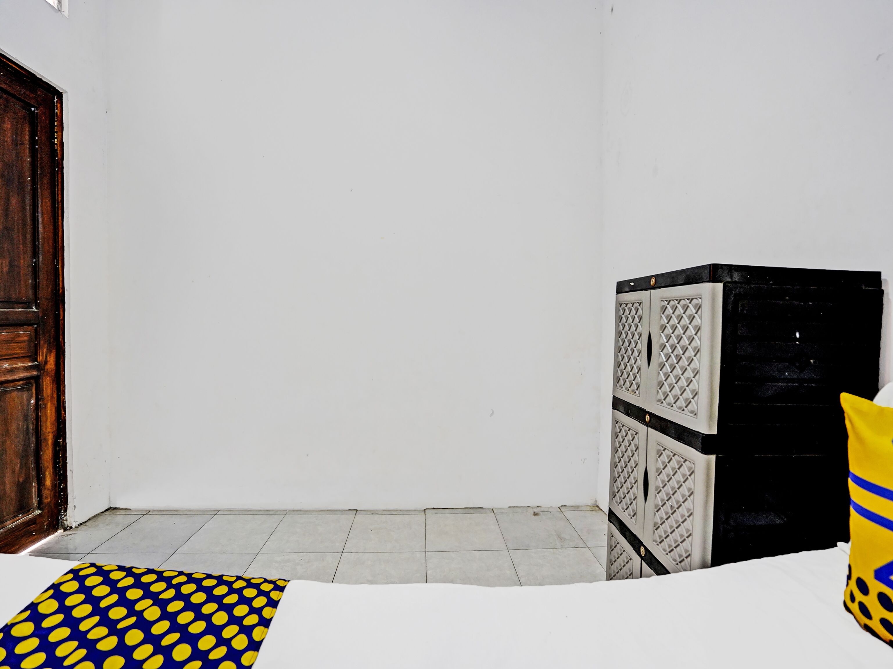 Una stanza con una porta di legno, un muro bianco, un pavimento piastrellato e un armadietto bianco e nero.