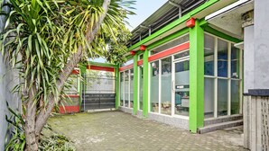 A building with green and red exterior walls, large windows, and a paved courtyard with a palm tree. - Hotel O Fun Guesthouse Syariah (Mojokerto)