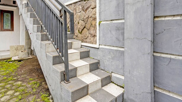 A staircase with metal railings leading to a building with a stone wall and a window. - Hotel O Fun Guesthouse Syariah (Mojokerto)