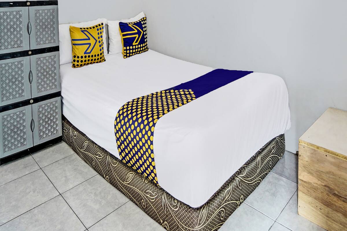 A neatly made bed with a white duvet, two pillows with geometric patterns, and a decorative throw.
