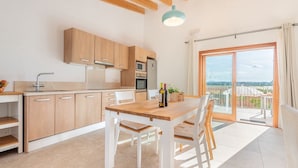 Een moderne keuken met houten kastjes, een eettafel en uitzicht op een balkon met een glazen deur.