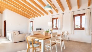Een ruime woonkamer met een houten eettafel, witte stoelen, een bank en een televisie.