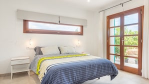 Een slaapkamer met een bed, nachtkastje, raam en deur.