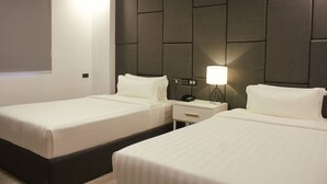 Habitación de hotel con dos camas, cabecera acolchada, mesitas de noche con lámparas y una ventana con persiana.