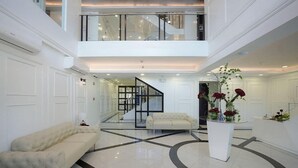 Un vestíbulo amplio con techo alto, una escalera central y un área de descanso con un sofá y una mesa de centro.