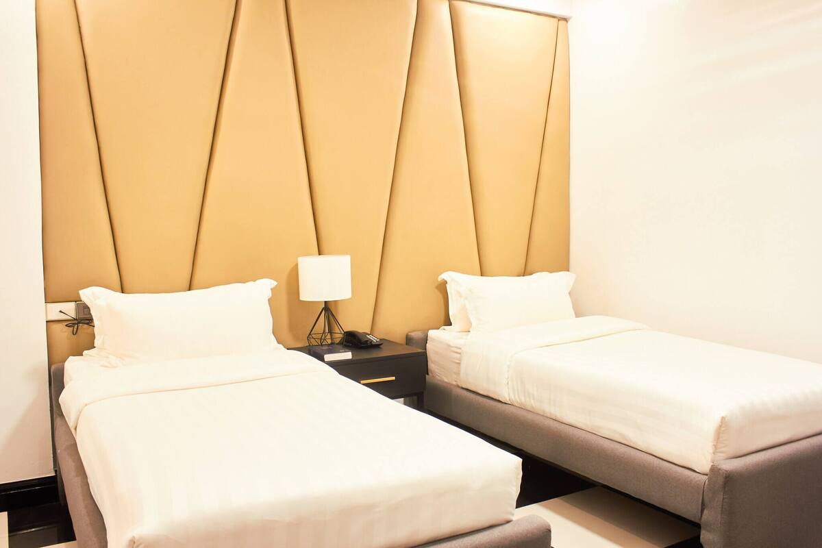 A hotel room with two beds, a nightstand with a lamp, and a phone.