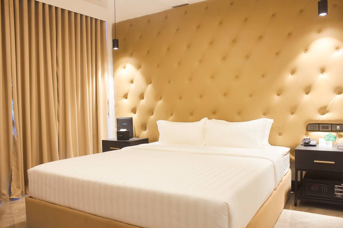 A hotel room with a large bed, a tufted headboard, a bedside table with a phone, and a nightstand with a lamp.