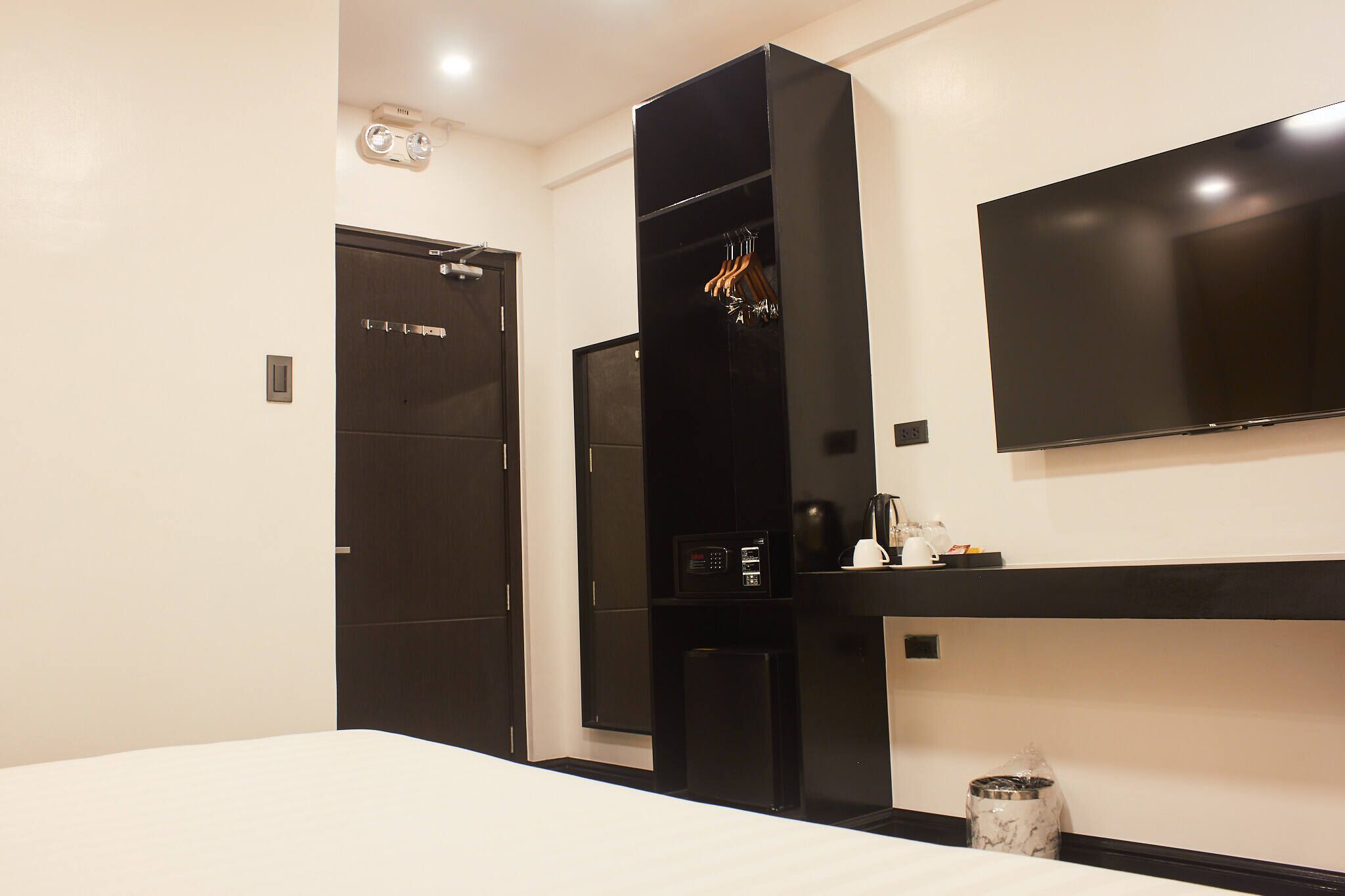 Una habitación de hotel moderna con una cama, un armario negro, un televisor de pantalla plana y una pequeña kitchenette.
