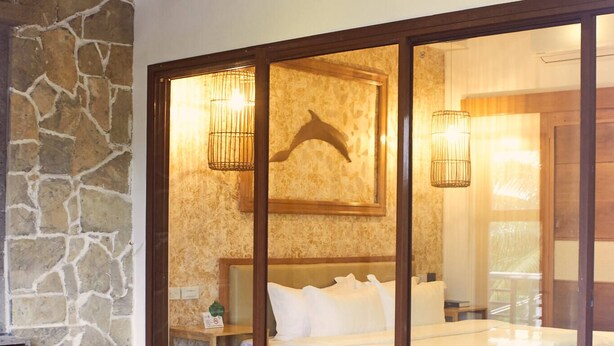 Una habitación con pared de piedra, cama con ropa blanca y techo de madera.