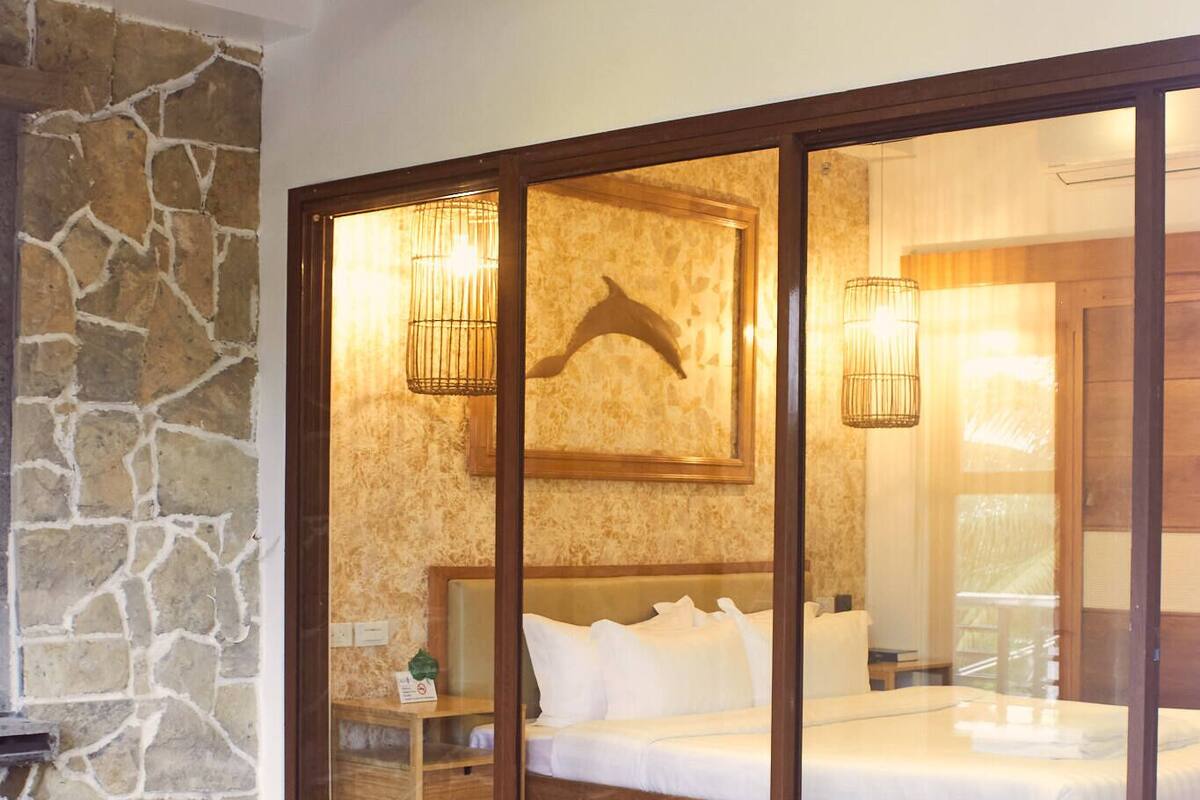 A room with a stone wall, a bed with white bedding, and a wooden ceiling.